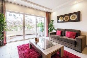 A modern living room with a sofa, a glass coffee table, and a large sliding glass door leading to a balcony. - Verasol N, 5 minutes from Praia dos Pescadores, Albufeira (Albufeira)