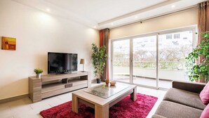 Un salon moderne doté d’un téléviseur à écran plat, d’une table basse en bois, d’un tapis rouge, d’un canapé et d’un balcon avec vue.