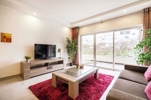 A modern living room with a flat-screen TV, a wooden coffee table, a red rug, a sofa, and a balcony with a view. - Verasol N, 5 minutes from Praia dos Pescadores, Albufeira (Albufeira)