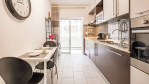 Une cuisine moderne avec un coin repas, une horloge au mur et une vue à travers la porte vitrée.