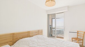 A bedroom with a bed, a chair, a window with a view, and a hanging light fixture. - Breathtaking ocean view, stay for 2 (Saint-Gilles-Croix-de-Vie)