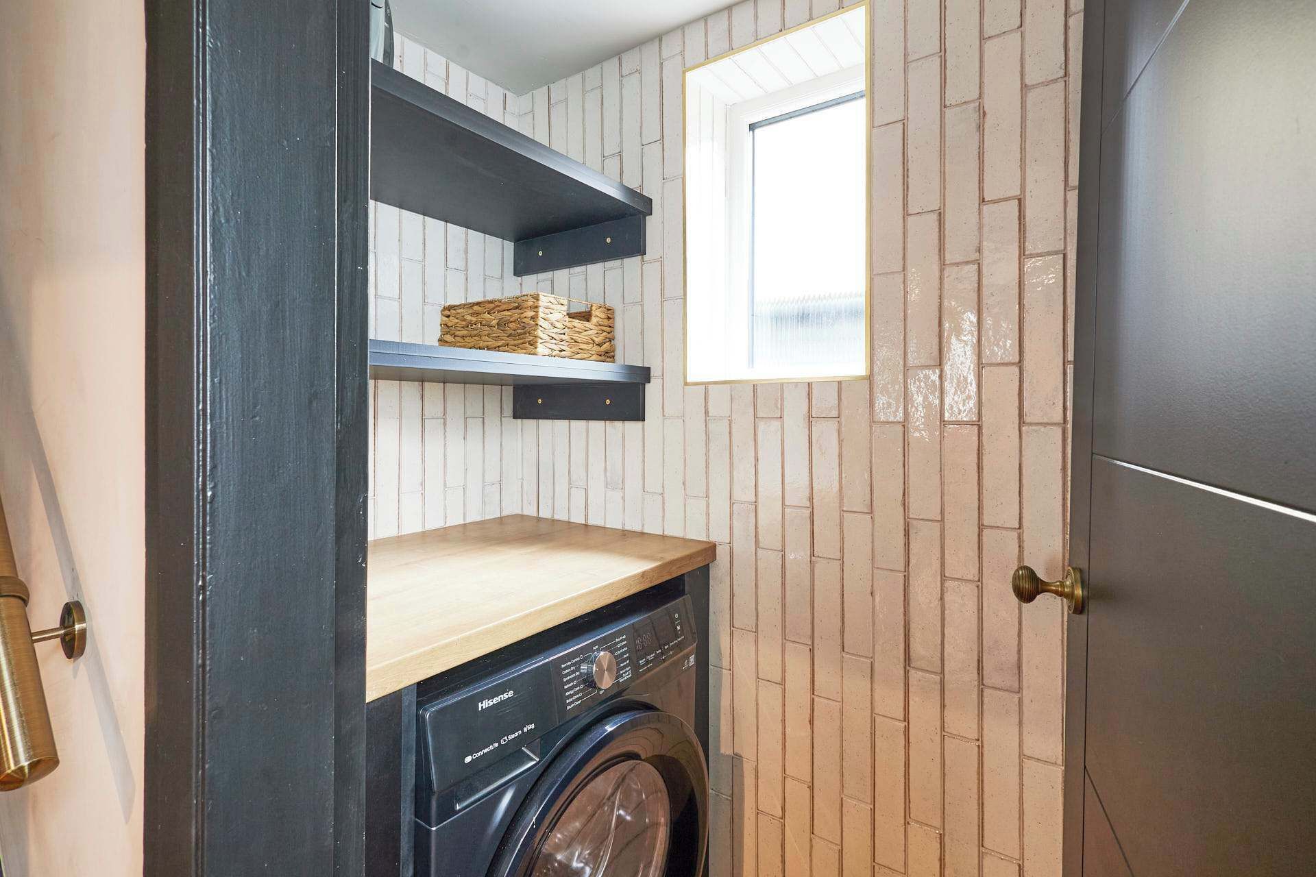 Une petite buanderie équipée d’un lave-linge, d’une étagère en bois et d’une fenêtre.