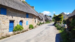 Eine enge Gasse, gesäumt von Steinhäusern mit Strohdächern und blauen Fensterläden.