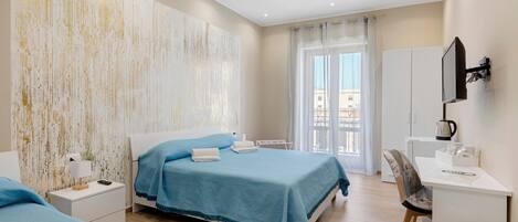 A hotel room with a bed, a desk, a chair, a TV, and a view of the city.