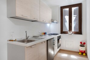 Eine Küche mit Spüle aus Edelstahl, einem Gasherd und einem Fenster mit Jalousien.