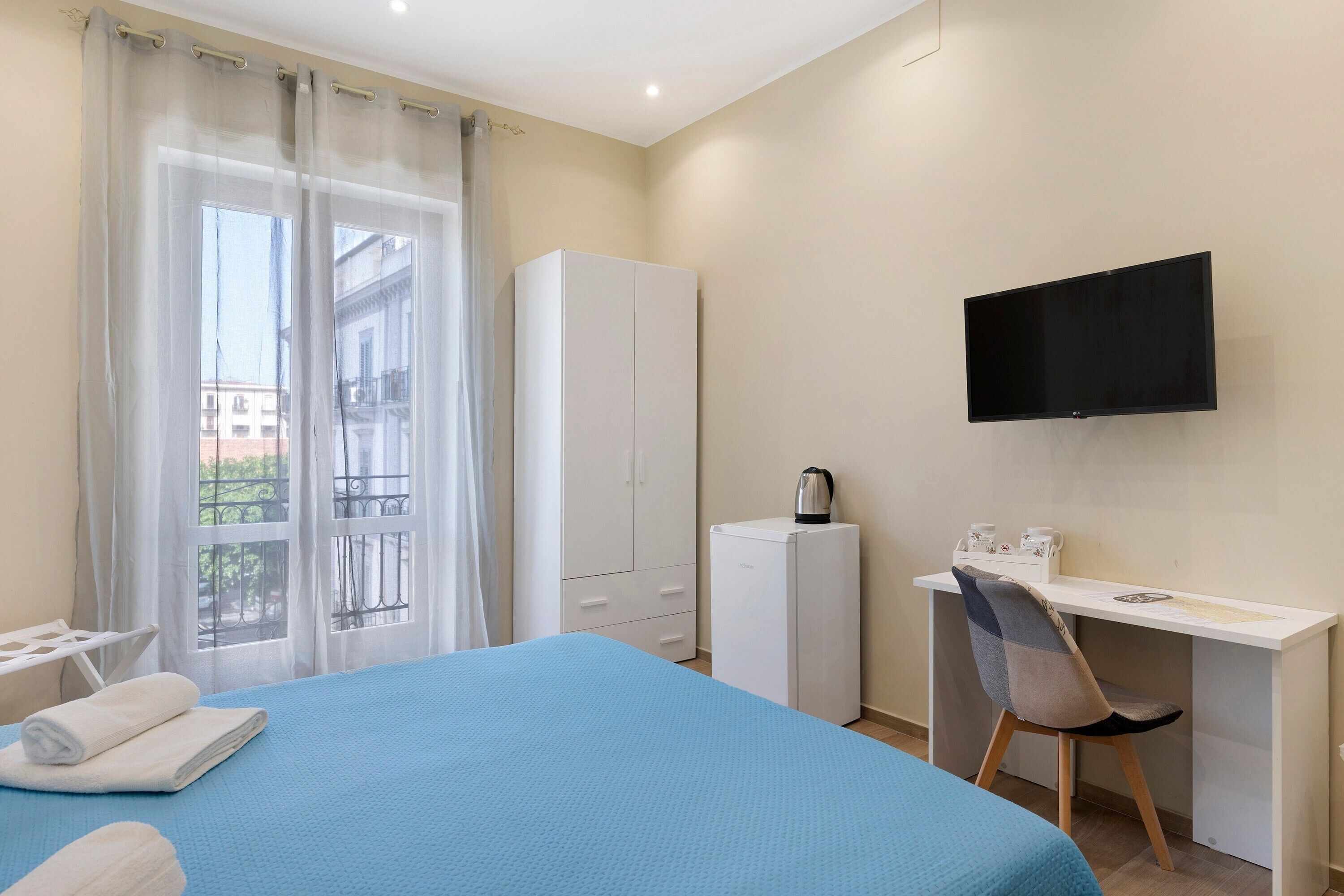 A hotel room with a bed, a desk, a television, a wardrobe, and a coffee machine.