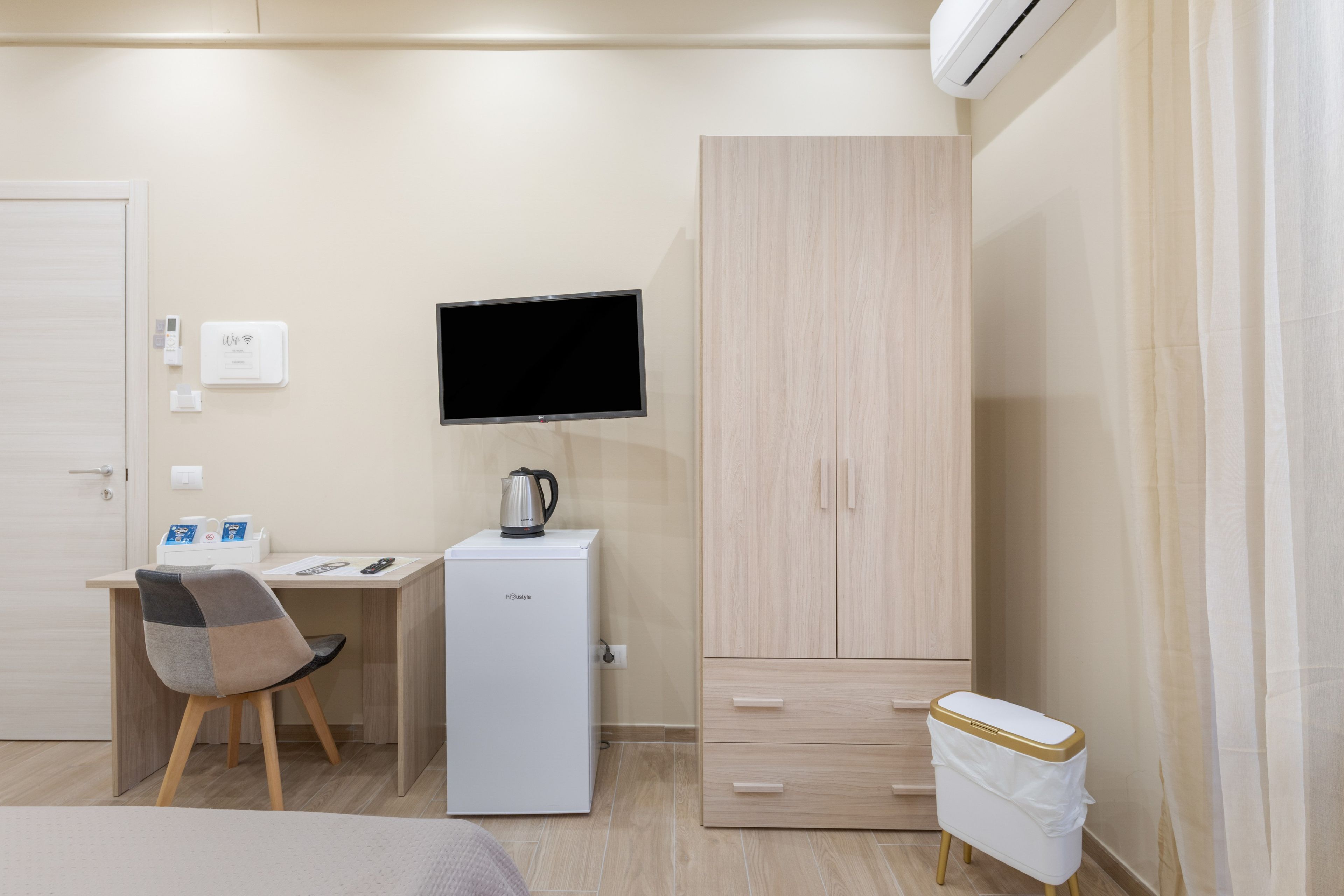 Ein kompaktes Hotelzimmer mit Bett, Schreibtisch mit Computer, Fernseher, Kleiderschrank und einer kleinen Küchenzeile.
