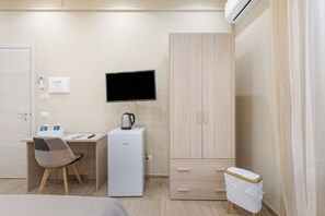 A compact hotel room with a bed, a desk with a computer, a TV, a wardrobe, and a small kitchenette. - Room 'Ferrovia' with Balcony, Wi-Fi and Air Conditioning (Palermo)