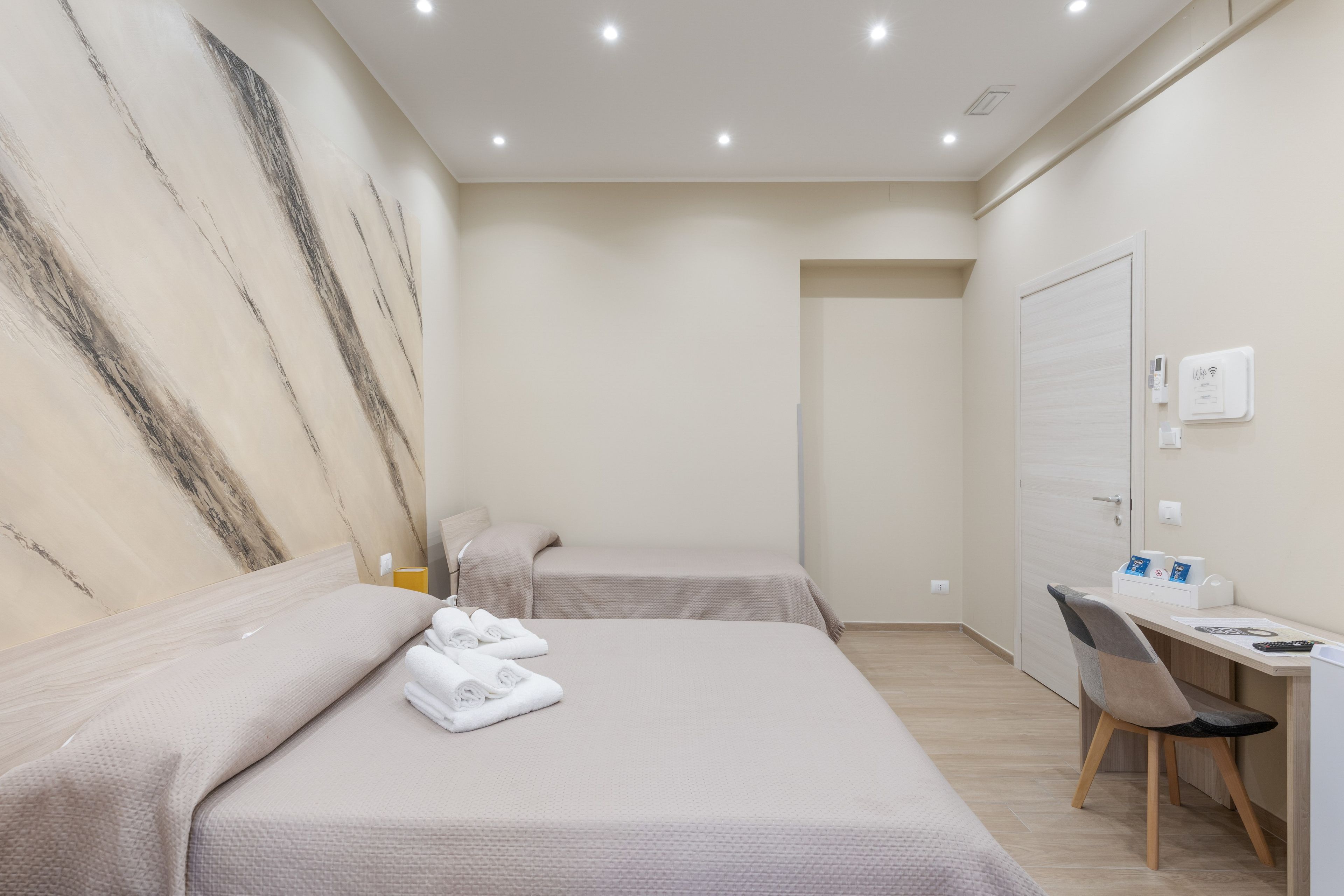 Une chambre d’hôtel avec deux lits, un bureau, une chaise et une station de recharge fixée au mur.