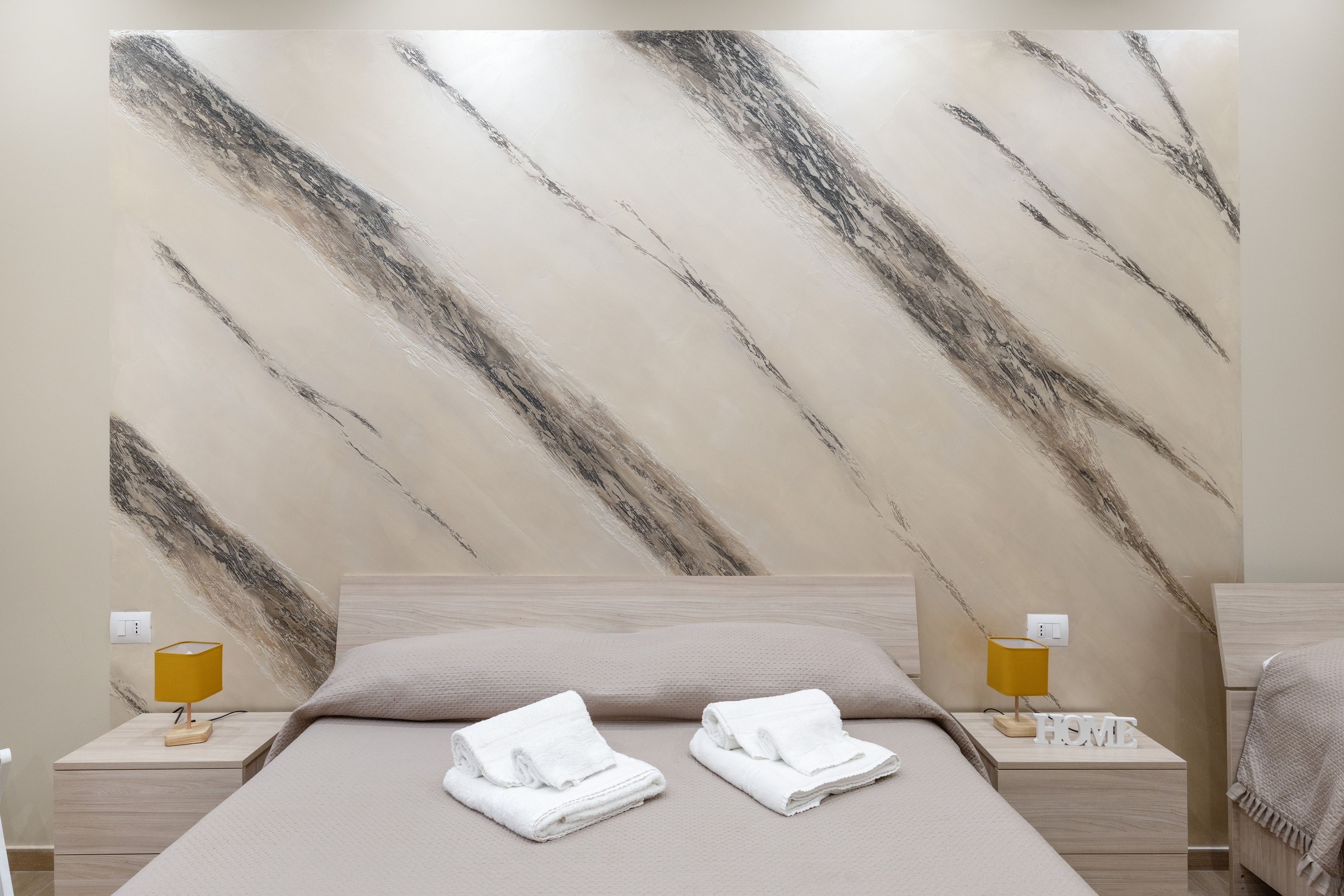 A hotel room with a bed, two nightstands, a lamp, and a wall with a marble-like pattern.