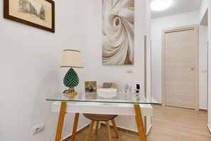 A room with a glass-top desk, a lamp, a decorative tree, a framed picture, and a door. - Room 'Ferrovia' with Balcony, Wi-Fi and Air Conditioning (Palermo)