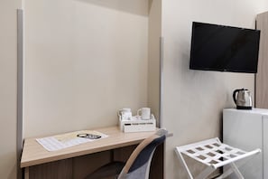 Ein Hotelzimmer mit einem Holztisch, einem weißen Stuhl, einem an der Wand befestigten Fernseher und einem kleinen Schrank mit einem Wasserkocher.