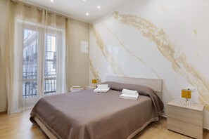Hotelkamer met een bed, nachtkastje met lamp, raam met gordijnen en een marmeren muur.