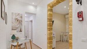 A modern interior with a glass dining table, a wooden chair, a wall with a textured column, and a red telephone. - Room 'Stazione' with Balcony, Wi-Fi and Air Conditioning (Palermo)