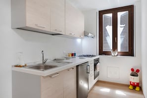 Een keuken met een roestvrijstalen spoelbak, een gasfornuis en een raam met zonwering.