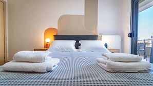 Ett hotellrum med en stor säng, två sängbord, ett litet bord, en lampa och utsikt genom en skjutdörr.