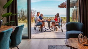 A dining area with a view of the beach, a table, chairs, and a large window.