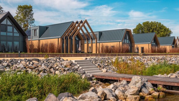 A modern building with large windows, a stone pathway, and a wooden deck over water.