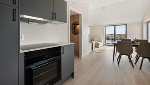 A modern kitchen with built-in appliances, a dining area with a table and chairs, and a view through a glass door. - Top apartment in Henningsvær (Vågan)