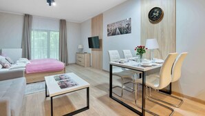 Ein modernes Hotelzimmer mit einem Bett, einem Essbereich mit Tisch und Stühlen, einem Fernseher und einer Uhr an der Wand.