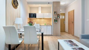 Ein modernes Wohnzimmer mit Essbereich, einer Küche mit weißen Schränken und einer Holztür.