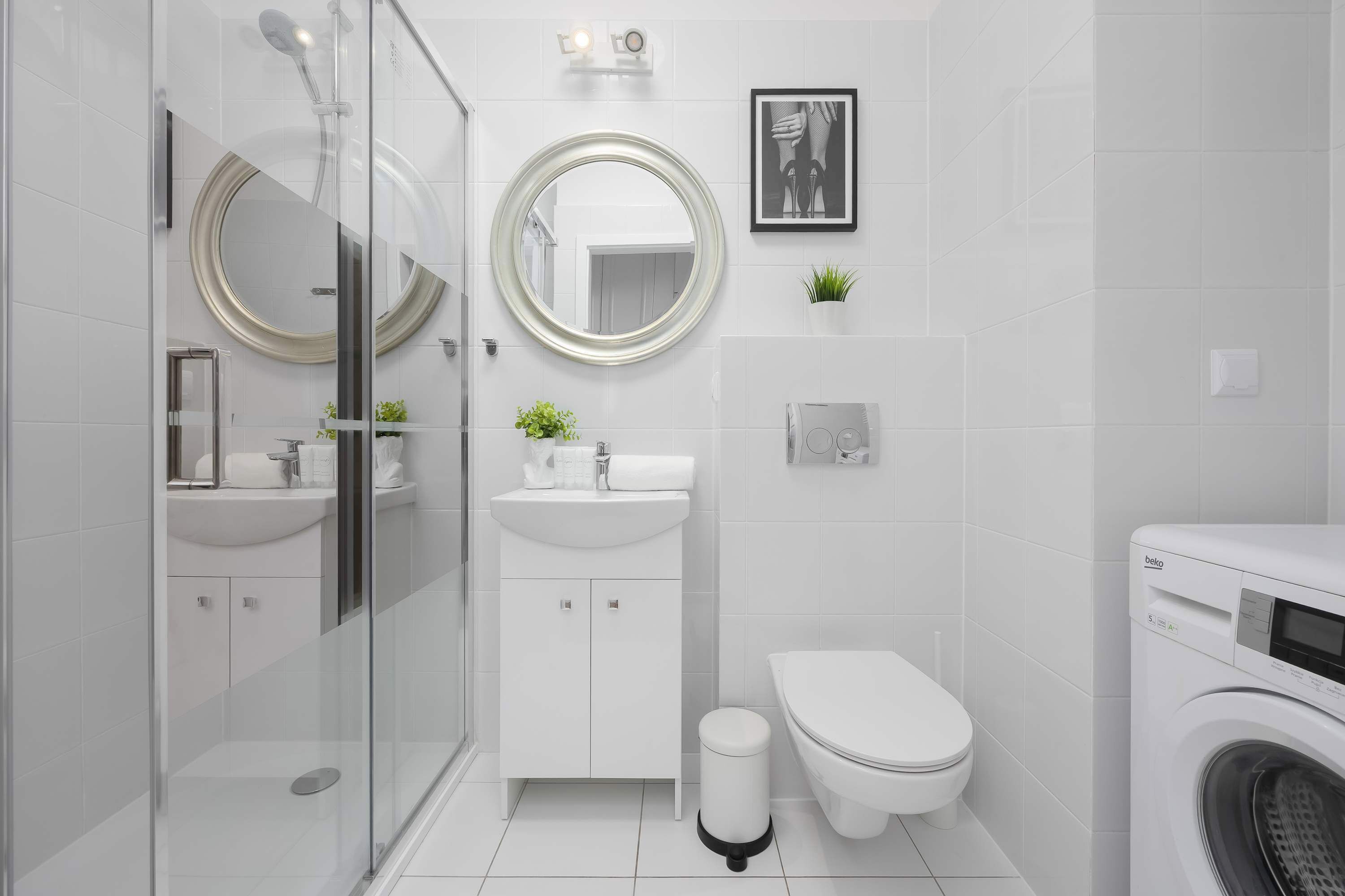 Une salle de bain moderne avec une douche à parois de verre, un miroir rond, des toilettes et un lave-linge.
