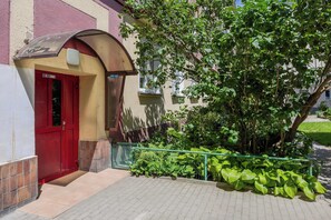 A building entrance with a red door, a covered awning, and a green railing. - Spacious Apartment for 6 Guests with a Bathtub in Warsaw by Noclegi Renters (Warszawa)
