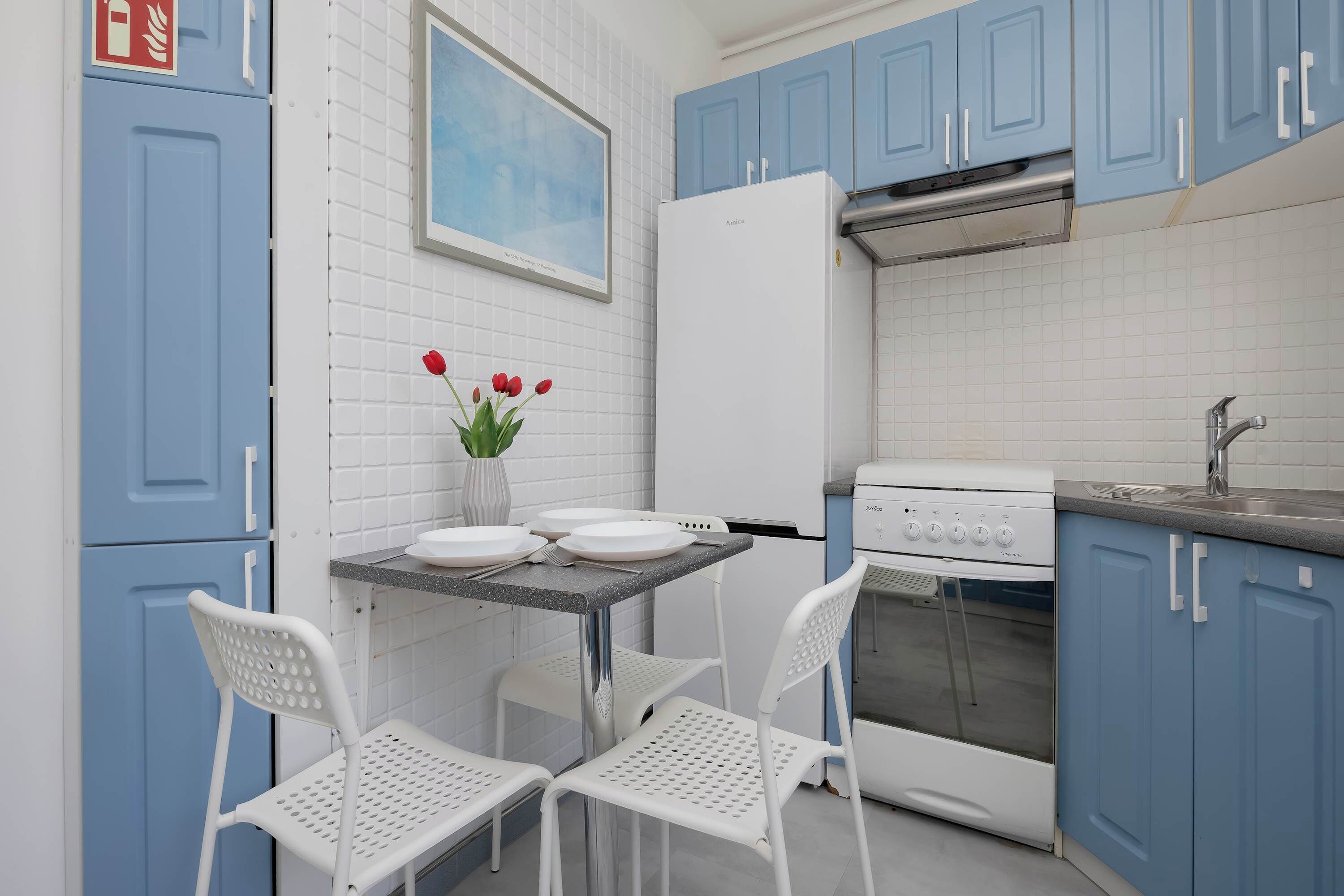A kitchen with blue cabinets, a white refrigerator, a stove, and two white chairs.