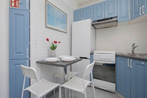 A kitchen with blue cabinets, a white refrigerator, a stove, and two white chairs. - Spacious Apartment for 6 Guests with a Bathtub in Warsaw by Noclegi Renters (Warszawa)