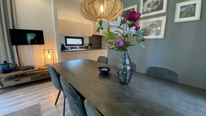 Een eethoek met een lange tafel, stoelen, een vaas met bloemen, een televisie en kunst aan de muur.
