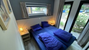 Een slaapkamer met een bed, nachtlampjes, een raam met gordijnen en uitzicht op buiten.