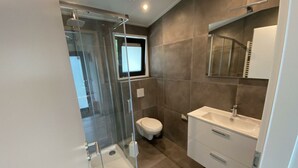 Een moderne badkamer met een douchecabine van glas, een toilet en een wastafel met spiegel.