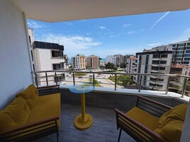 Un balcón con mobiliario amarillo, una mesa redonda y vistas de un paisaje urbano con edificios y cielo despejado.