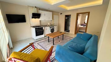 A compact living space with a kitchenette, a sofa, a wooden table, and a chair.