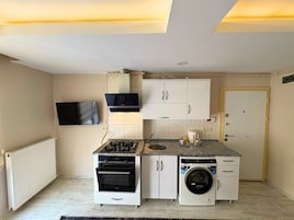 Cozinha compacta com forno embutido, micro-ondas e máquina de lavar roupa, TV fixada na parede e porta com puxador.