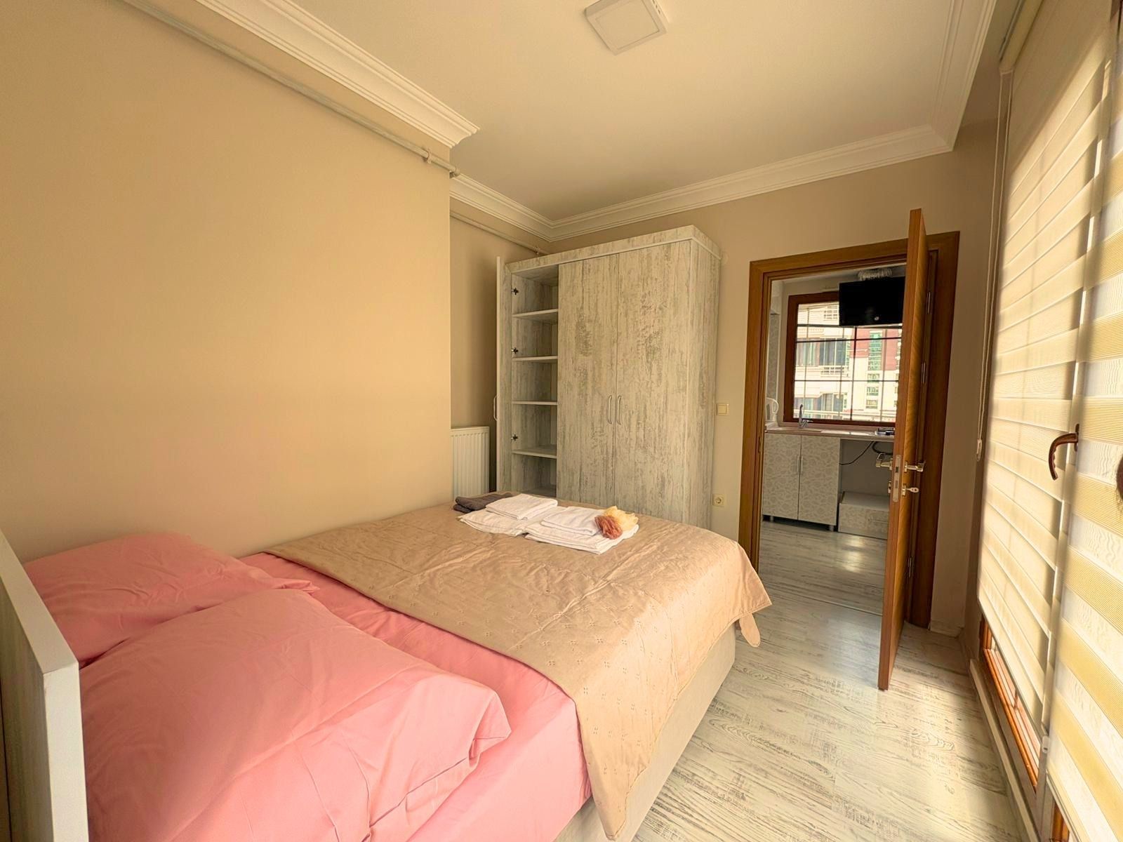 A bedroom with a bed, a wardrobe, and a view into the kitchen.
