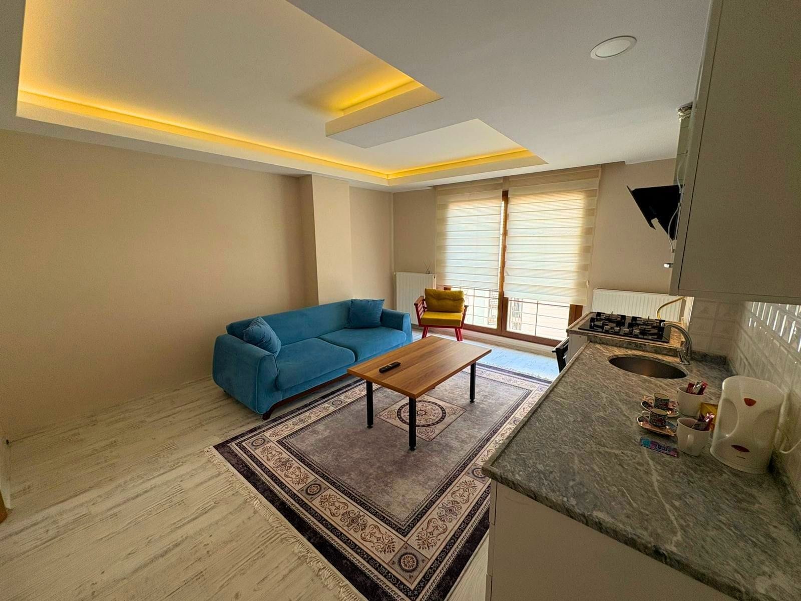 A modern living room with a sofa, a coffee table, and a kitchen area with a stove and sink.