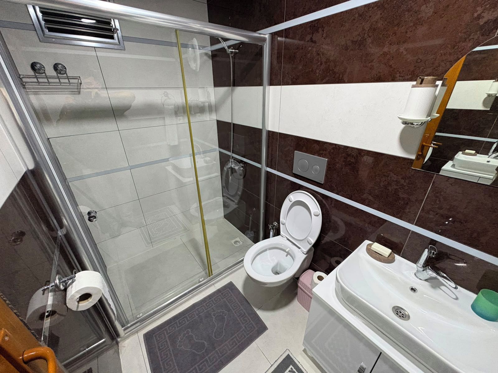 A bathroom with a glass-enclosed shower, a toilet, a sink, and a mirror.
