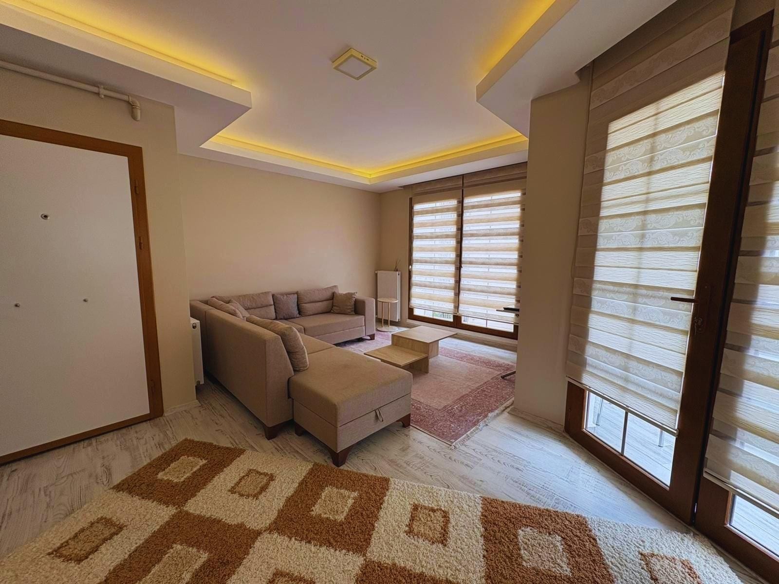 A modern living room with a sectional sofa, a coffee table, and a patterned rug.