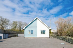 A small, single-story house with a gabled roof, a fenced yard, and a clear sky. - Moranedd Bach (Holyhead)