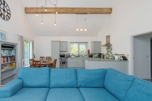 Ein modernes Wohnzimmer mit blauem Sofa, einem Essbereich mit Tisch und Stühlen, einer Küche mit Waschmaschine und einem großen Fenster.