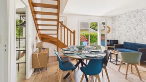 Un coin repas avec un escalier en bois, une table dressée pour quatre personnes et un canapé bleu dans le salon.