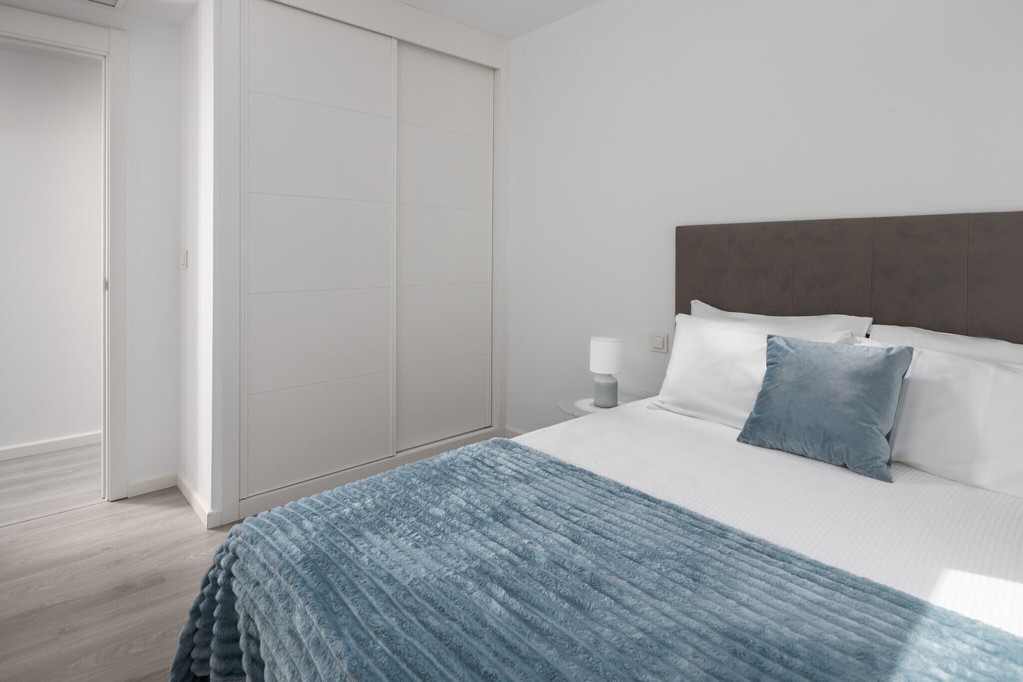 Un dormitorio con cama, mesita de noche, lámpara y armario.