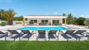 Una casa moderna con piscina, mobiliario exterior y terraza cubierta.