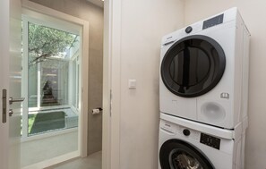 A compact laundry room with a front-loading washer and dryer, a glass door leading to a balcony, and a white tiled wall. - Stunning home in Pridraga (Pridraga)