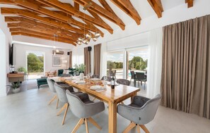 A spacious dining area with a wooden table and grey upholstered chairs, a modern kitchen with wooden beams, and a large window overlooking a pool. - Stunning home in Pridraga (Pridraga)