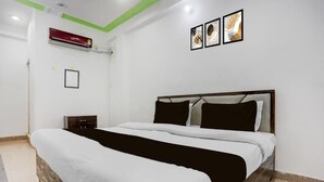 A bedroom with a bed, a nightstand, an air conditioning unit, and framed artwork on the wall. - Hotel kartikey (Phulpur)