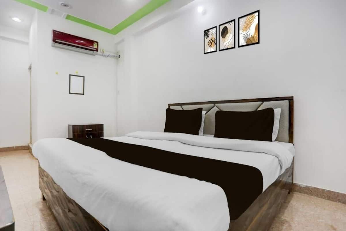A bedroom with a bed, a nightstand, an air conditioning unit, and framed artwork on the wall.
