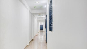 A long, narrow hallway with white walls, a tiled floor, and a blue window on the right. - Hotel kartikey (Phulpur)
