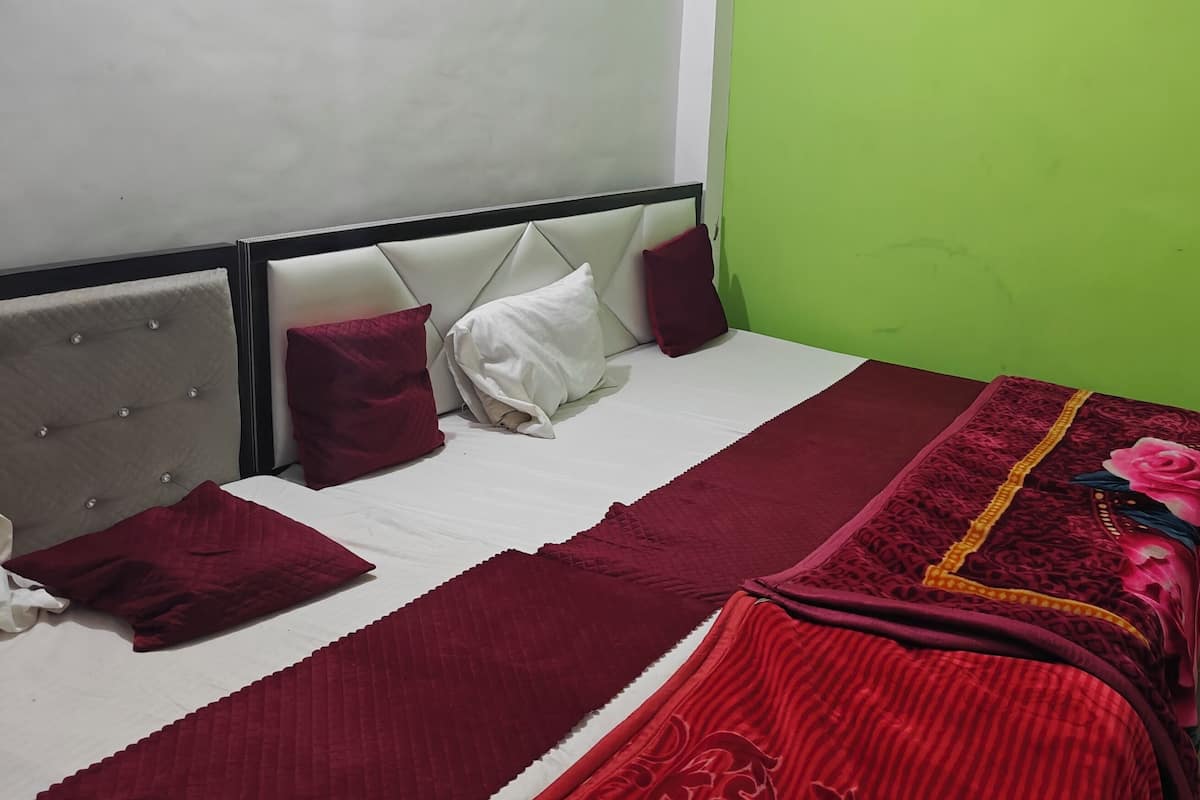 A single bed with a white headboard, red and white bedding, and a green wall.